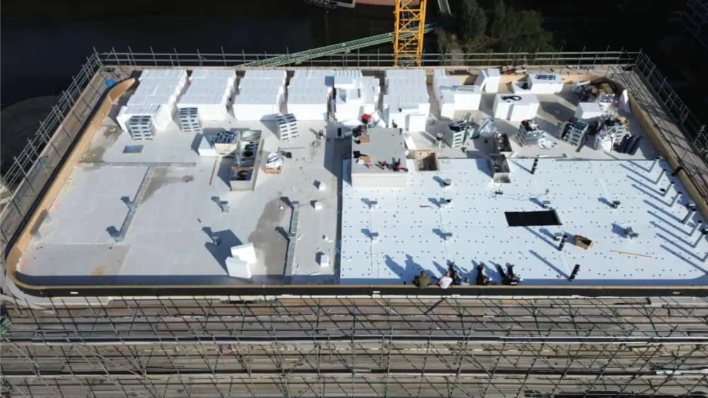 Installatie van witte isolatiepanelen op een plat dak (Platte daken) met steigers en bouwkraan op de achtergrond