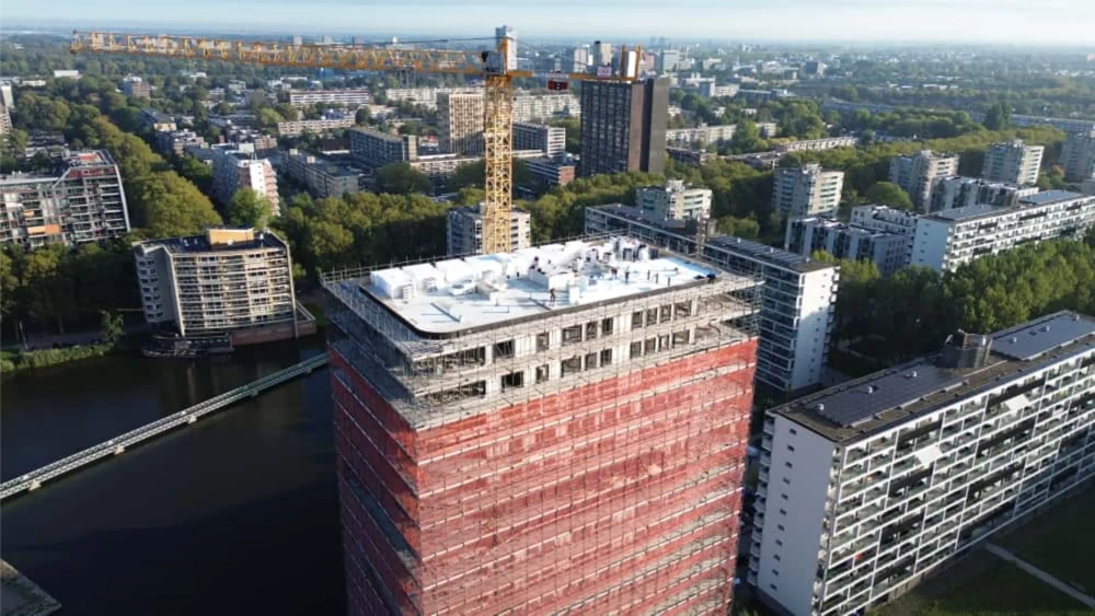 Bovenaanzicht van flatgebouw met steigers, kraan en monteurs tijdens Dakrenovatie van een plat dak