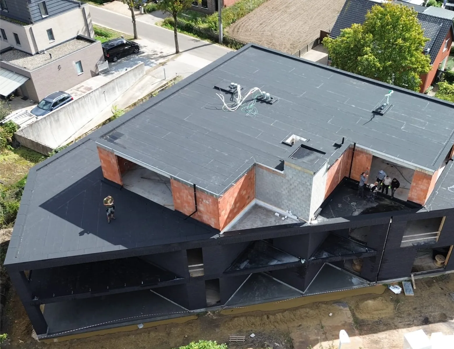 Werknemers voeren dak waterdicht maken uit op plat dak van nieuwbouw met zwarte membraanlaag
