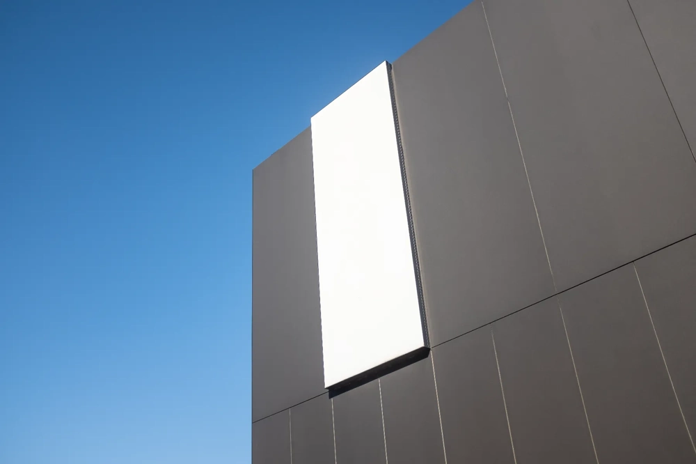 Zwart metalen gevel met opvallend wit paneel onder helderblauwe lucht