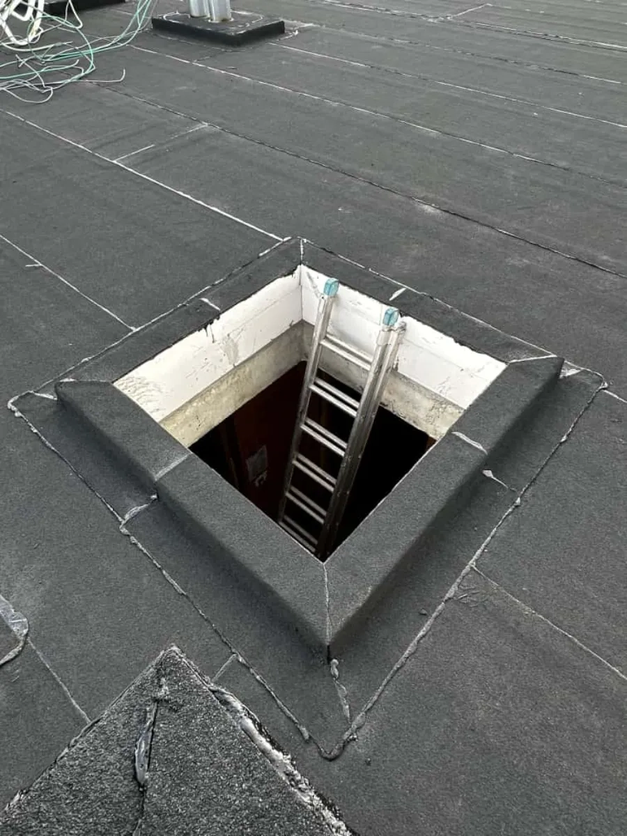 Nieuw dakluik in plat bitumen dak met metalen ladder naar binnen