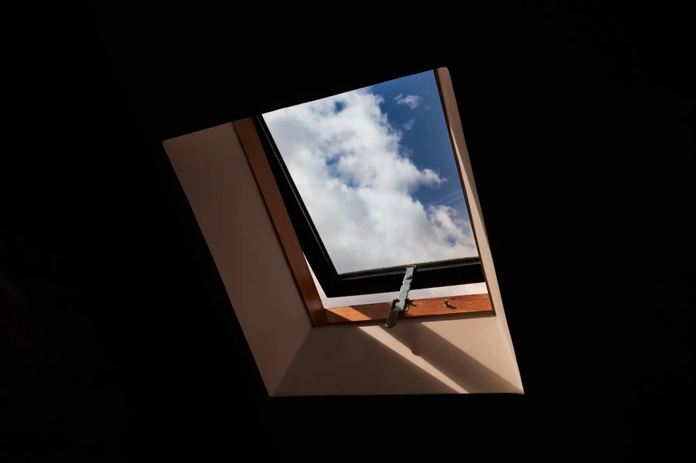 Openstaand dakraam (Dakramen) in houten kozijn boven zolder met zicht op blauwe hemel en witte wolken